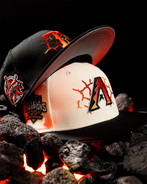 Two Arizona Coyotes baseball caps displayed on dark rocks with glowing embers. One cap is black with a large Arizona logo and World Champions 2026 patch, and the other is white with a black brim and Arizona logo, both styled over a black background.